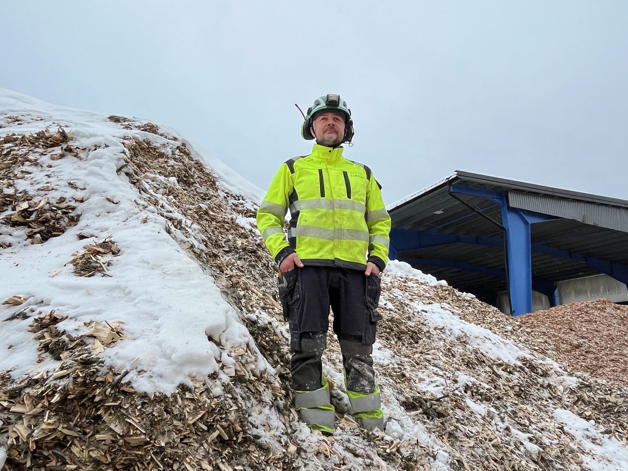 Mann i vernetøy står i snødekt flishaug