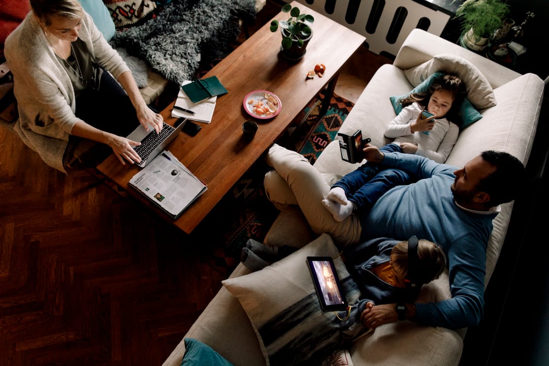 Familie hjemme i stuen som bruker bredbånd til streaming, jobb på laptop, nettbrett og mobil.